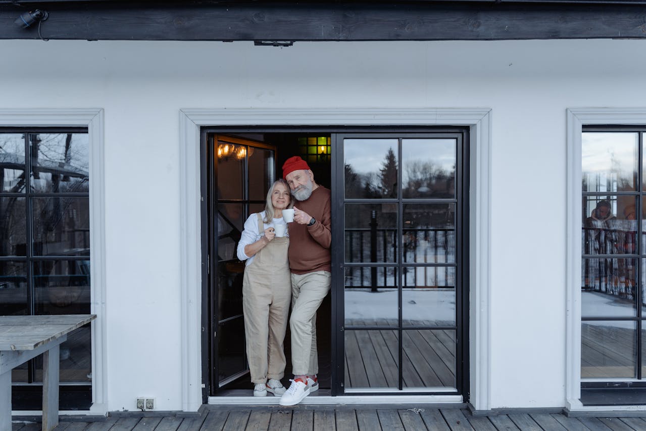 An elderly couple is standing at the door to their new home, purchased thanks to mortgages for seniors and retirees.