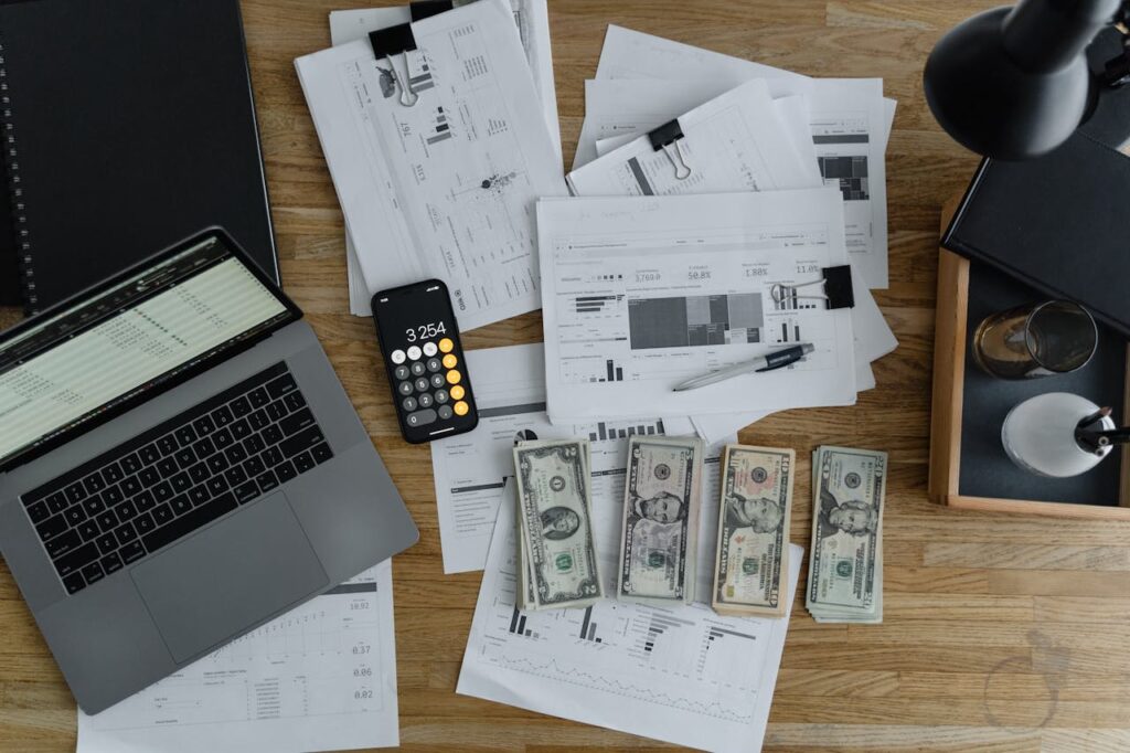 A top-down view of a desk with a laptop, paperwork, a phone calculator, and cash where someone is preparing their application for home loans for healthcare workers.