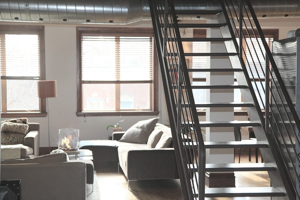 The interior of an apartment living room with stairs to the right and couches to the left. 