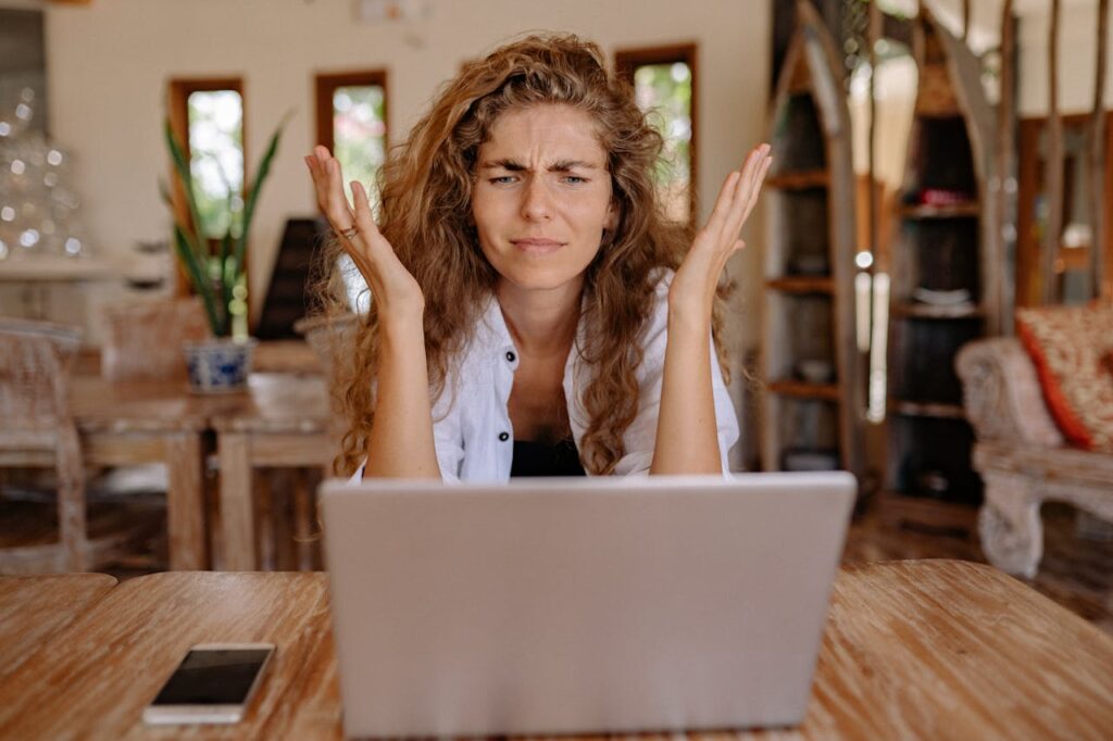 A woman has her hands up in front of her computer, frustrated at how high interest rates have gotten. 