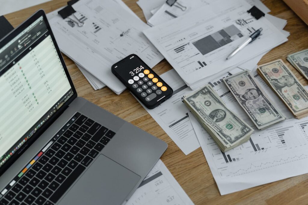 A laptop with cash and an iPhone calculator on a desk used to calculate mortgage closing costs.