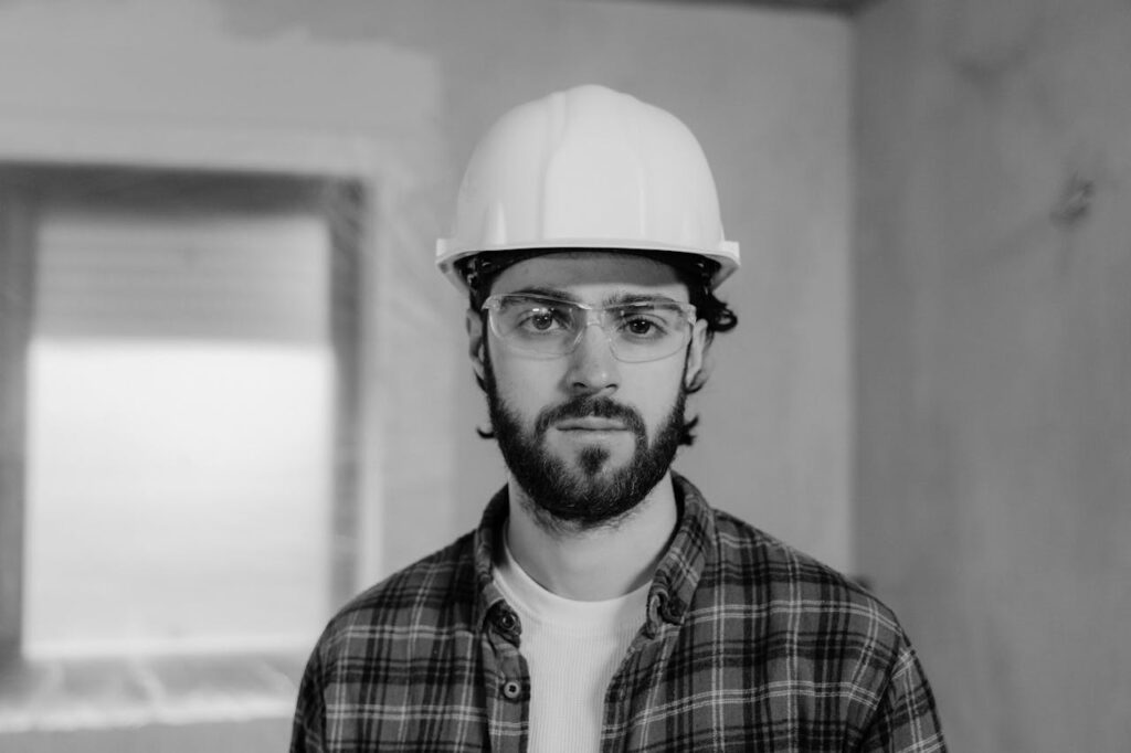 An inspector is looking at the camera while wearing a hard hat and safety glasses during a home inspection.