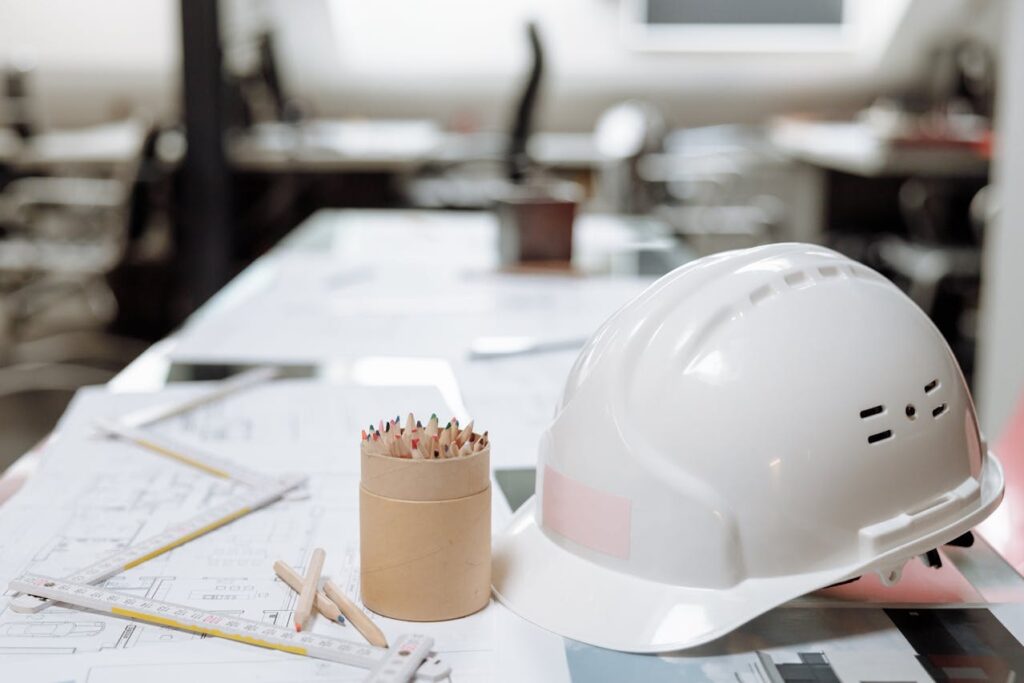 Construction plans with colored pencils and a white hard hat on top. 