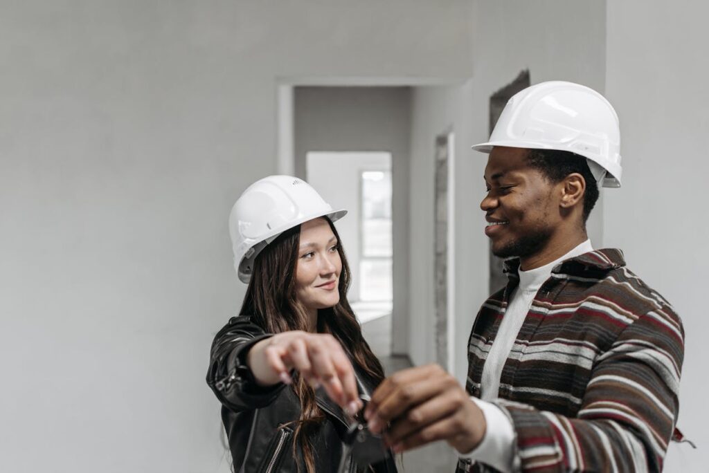 A young couple wearing white hard hats is holding the keys to their new-build home that was financed with a construction loan Oregon. 