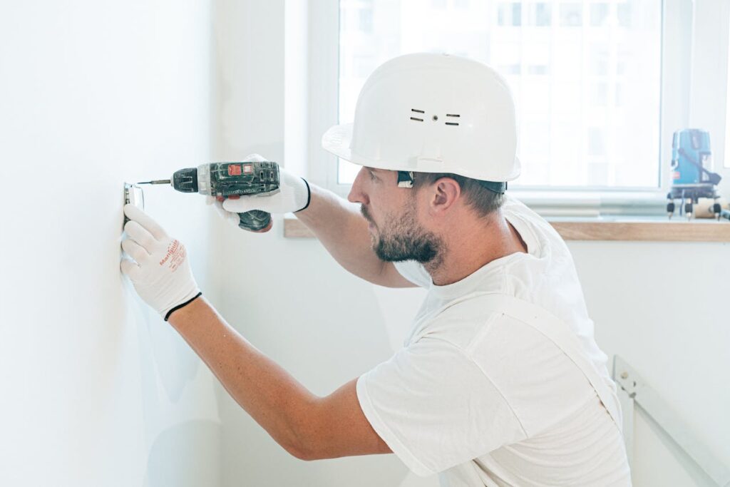 A handyman wearing a hardhat is drilling a hole in the wall of a home financed with a construction loan Texas.