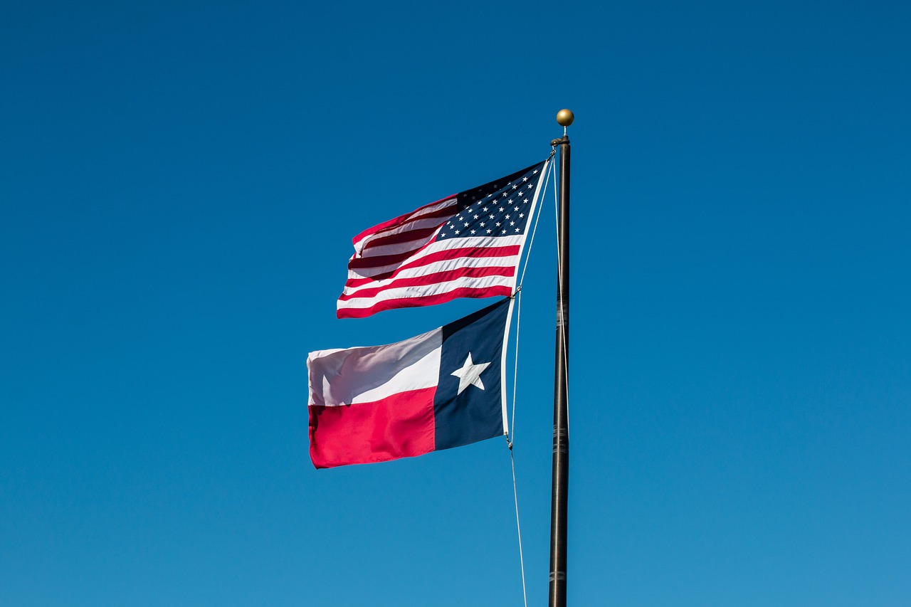 An American flag flying above a Texan flag against a clear blue sky, representing the journey of securing a construction loan Texas.