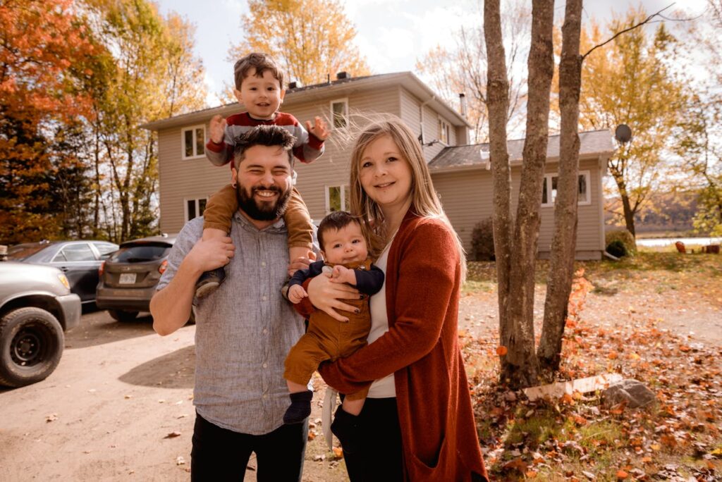 A young couple with two young children are standing in front of their new home. 