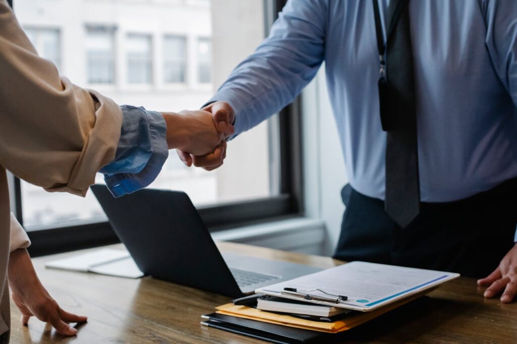 A loan officer is shaking hands with a new homeowner after paperwork was completed and explaining the difference between deed of trust vs mortgage. 