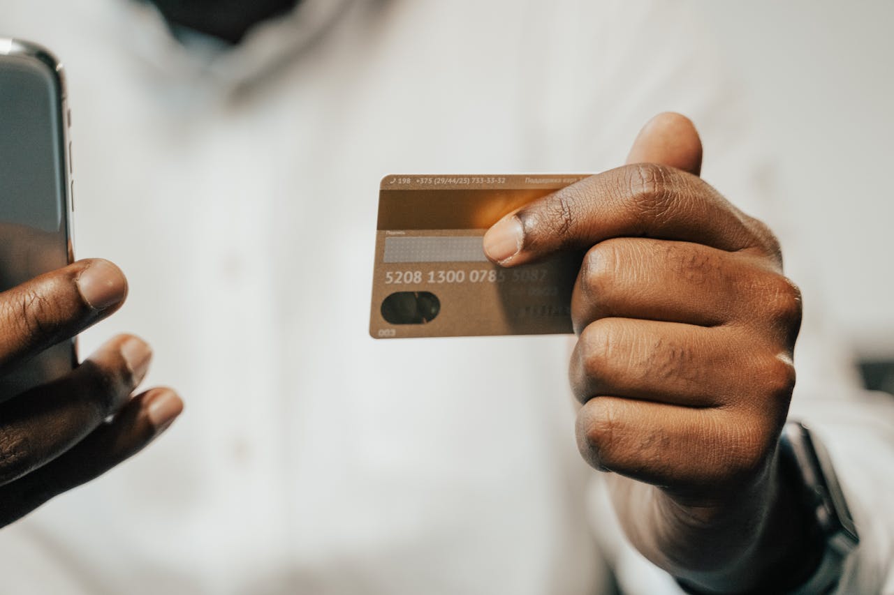 A man is holding a credit card and cell phone to make an online purchase after the Federal Reserve interest rate cut.